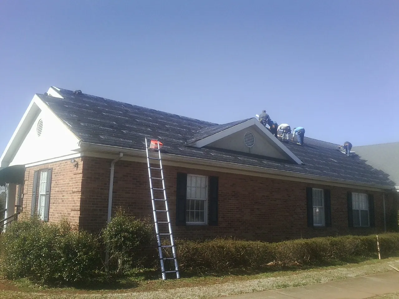 Crew tearing shingles off a brick ranch roof with a ladder set — Metal Roof Repair work by our crew in Bruceton Mills