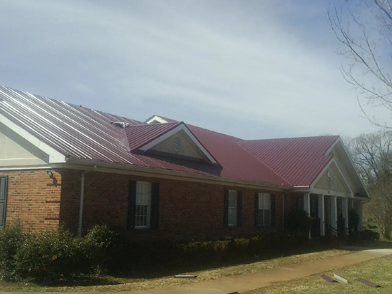 Red metal roof with gabled entries on a long brick building, from a Hail Damage Roof Repair job in Bruceton Mills