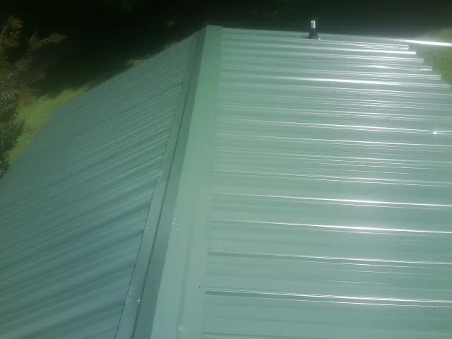 New green metal panels meeting at the ridge of a roof — Flat Roof Repair work by our crew in Bruceton Mills