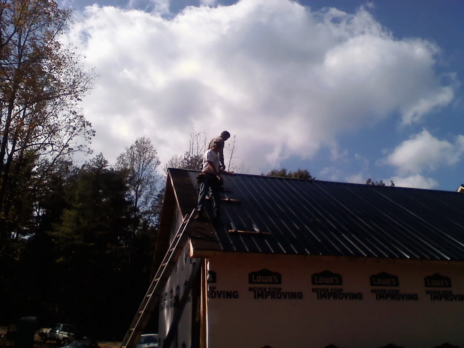 Roofer fastening dark metal panels high against a cloudy sky, from a Roof Inspection job in Bruceton Mills