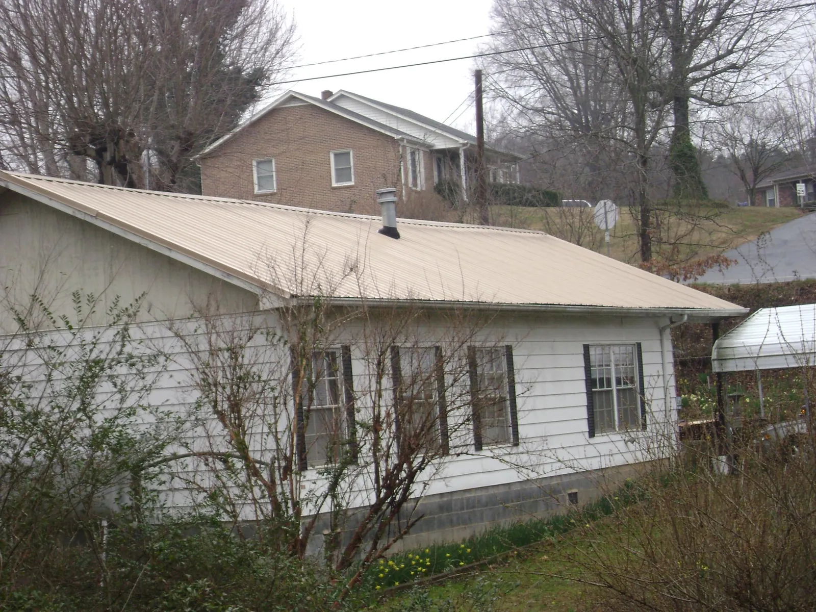 Tan metal roof on a white sided house set into a hillside — Commercial Roofing by Roofing Brothers in Bruceton Mills